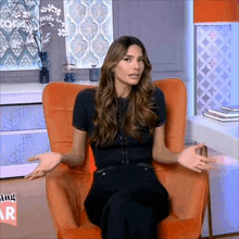 a woman is sitting in an orange chair with her arms outstretched in front of a sign that says nothing