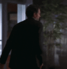 a man in a suit says bye in front of a plant