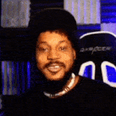 a man with a beard and a hat is smiling while wearing a black shirt and a necklace .