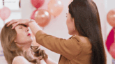 a woman touches another woman 's forehead in front of balloons and the words " i love you " on the bottom