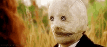 a man in a suit and tie is wearing a scarecrow mask with buttons on his eyes .