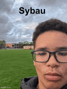 a young man wearing glasses is standing in front of a field with sybau written on the bottom