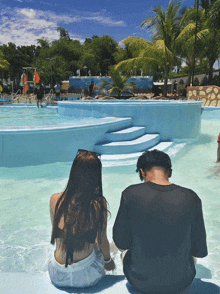 a man and a woman sit on the edge of a pool looking at the water