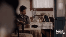 a man sits at a table with a cup of coffee in front of a sign that says heart & home