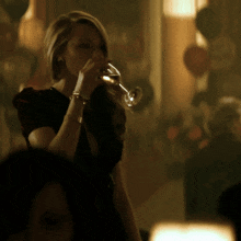 a woman in a black dress drinks from a glass