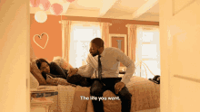 a man sits on a bed next to a woman who is laying on a bed and says " the life you want "