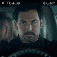 a man with a beard is driving a car with wildcards written on the bottom