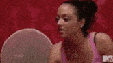 a woman in a pink tank top is looking at herself in a mirror with a mtv logo on the bottom right