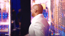 a man in a white suit is standing in front of a nbc sign