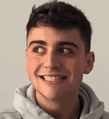 a young man wearing a white hoodie is smiling and looking to the side .