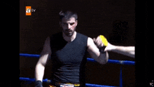 a man in a black tank top holds his arms up in the air with a tv logo behind him