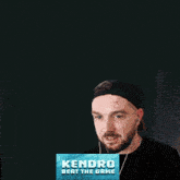 a man covering his face with his hand with a kendra beat the game sign in front of him