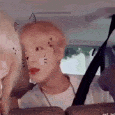 a man is sitting in the back seat of a car with a cat face painted on his face .