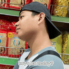 a man wearing a black hat is standing in front of a shelf of noodles with the words kaya ba today below him