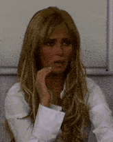 a woman with long blonde hair is wearing a white shirt and covering her mouth with her hand