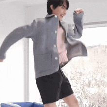 a young man in a gray jacket and black shorts is dancing in a room .