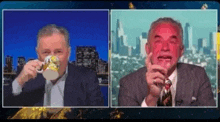 a man in a suit is drinking a cup of coffee while another man with a red face is smoking a cigar .