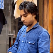 a man in a blue denim shirt looks down at something