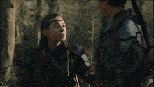 a man with a bow and arrow looks at a woman with a headband on