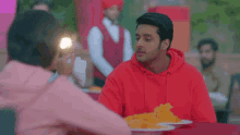 a man in a red hoodie is sitting at a table with a woman in a pink shirt .