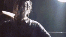 a man with dreadlocks is standing in a dark room holding a knife in his hand .