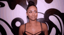 a woman in a black dress is smiling in front of a wall with a painting on it .
