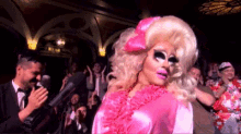 a drag queen in a pink dress is standing in front of a crowd .