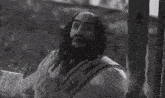 a black and white photo of a man with dreadlocks and a beard holding a stick