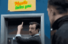 a man giving the middle finger in front of a sign that says mantle loves you .