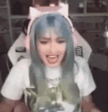 a woman with blue hair is wearing headphones and a cat ear headband while sitting in a chair .
