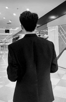 a black and white photo of a man in a suit with the word soon on the wall behind him
