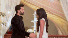 a man in a suit and a woman in a white dress are standing next to each other and holding hands .