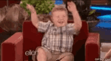 a young boy is sitting in a chair with his hands in the air .