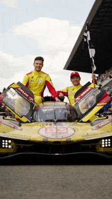 two men are standing in front of a yellow race car that says orlen on the front