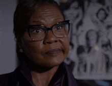 a woman wearing glasses and a purple shirt is looking at the camera