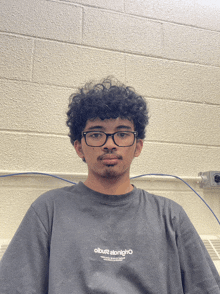 a young man wearing glasses and a t-shirt that says olbus2 stonighto looks at the camera
