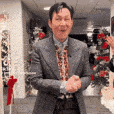 a man in a suit and tie is standing in front of a christmas tree and clapping .