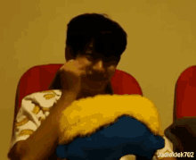 a man is sitting in a red chair with a stuffed animal on his lap and eating something .