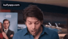 a man in a blue shirt is making a funny face while standing in a room .