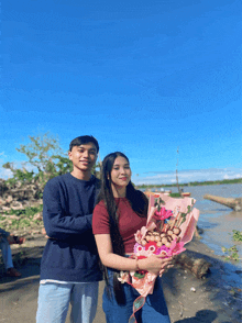 a man and a woman holding a bouquet of flowers in front of a body of water