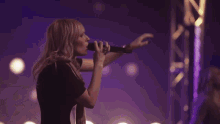 a woman singing into a microphone with a spotlight in the background