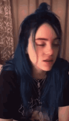 billie eilish has blue hair and is wearing a black t-shirt .