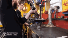 two men working on a machine in a hacksmith industries shop