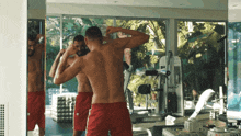 a shirtless man in red shorts is looking at himself in a mirror