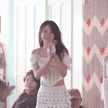 a woman in a white dress is standing in front of a group of people and clapping .