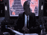a man in a suit sits at a desk in front of a map