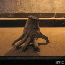 a statue of a hand with stitches on it sits on a table with netflix written on the bottom
