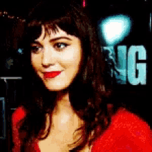 a woman in a red shirt is smiling in front of a sign that says ng