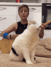 a woman is playing a guitar while a cat licks her face