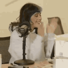 a woman with blue hair is sitting at a table in front of a microphone with her hands in the air .